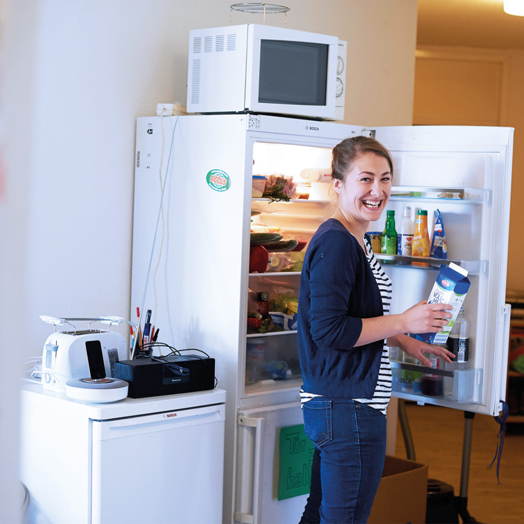 Das Bild zeigt eine junge Frau vor einem offenen Kühlschrank